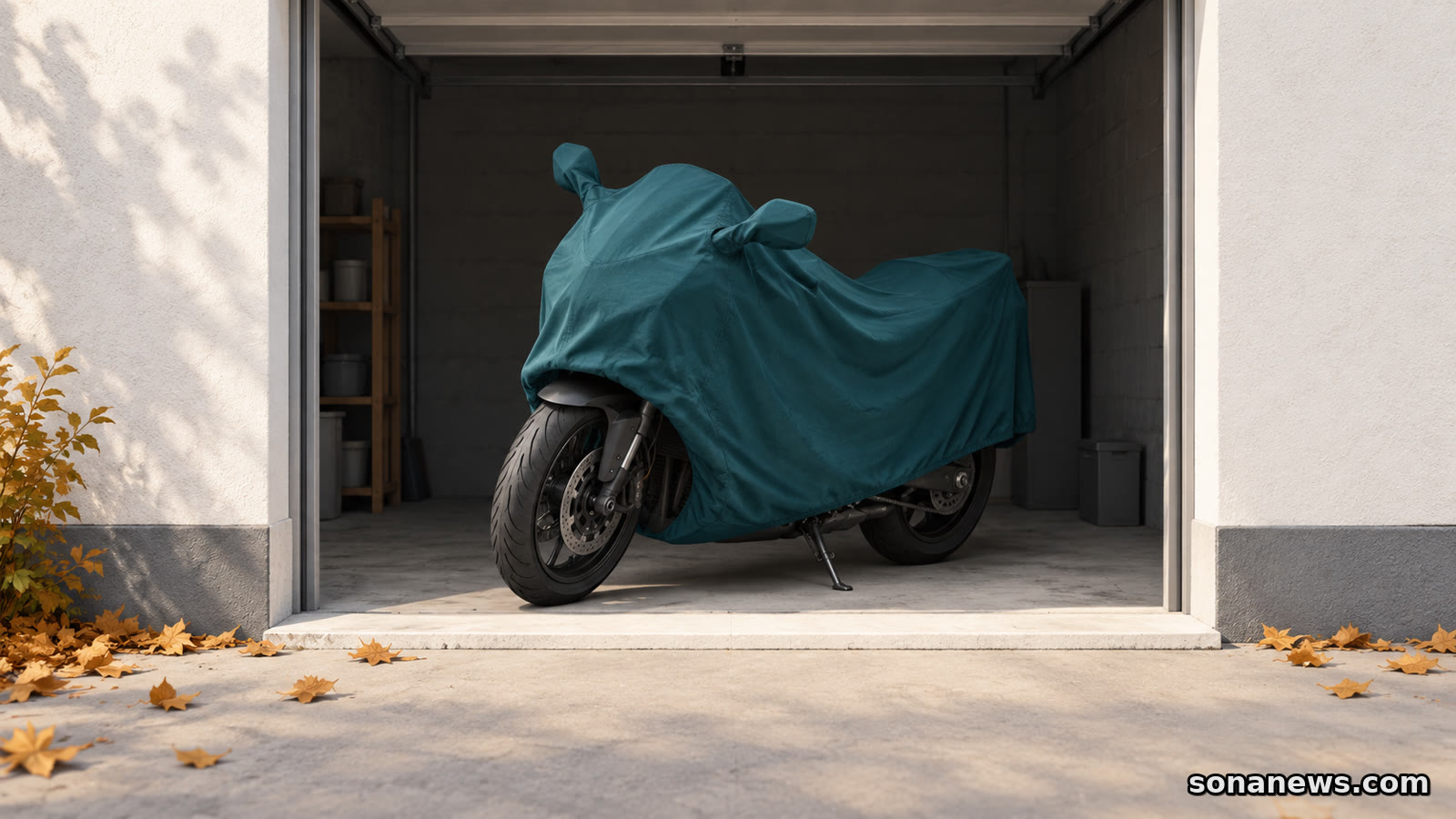Ein Motorrad unter einer petrolfarbenen Plane steht innerhalb einer Garage; vor der Schwelle liegen Herbstblätter als Hinweis auf die Saisonpause.