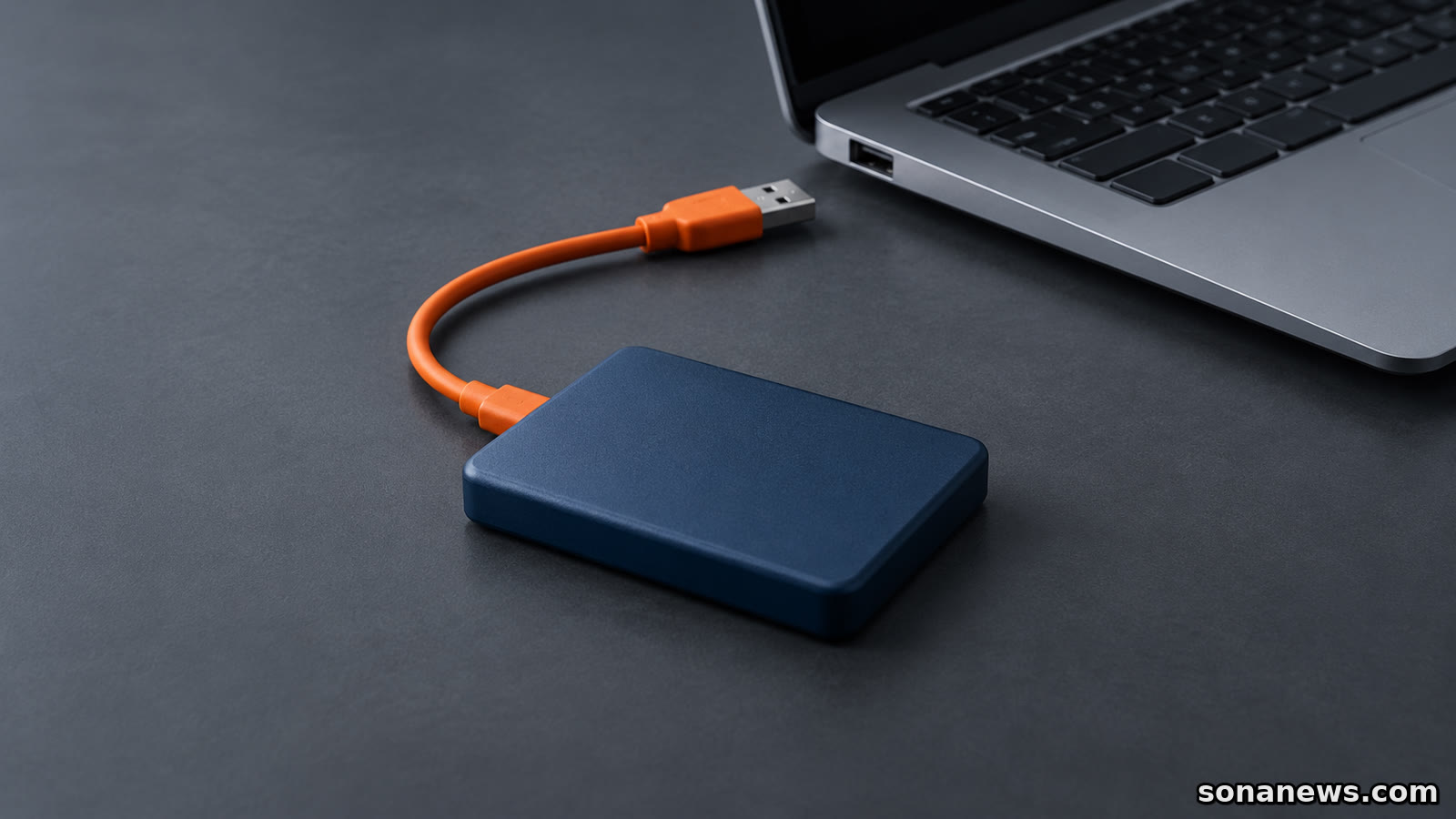 Externe Festplatte für ein Backup mit orangefarbenem Kabel; der freie USB-Stecker liegt sichtbar getrennt vom Anschluss eines Computers.
