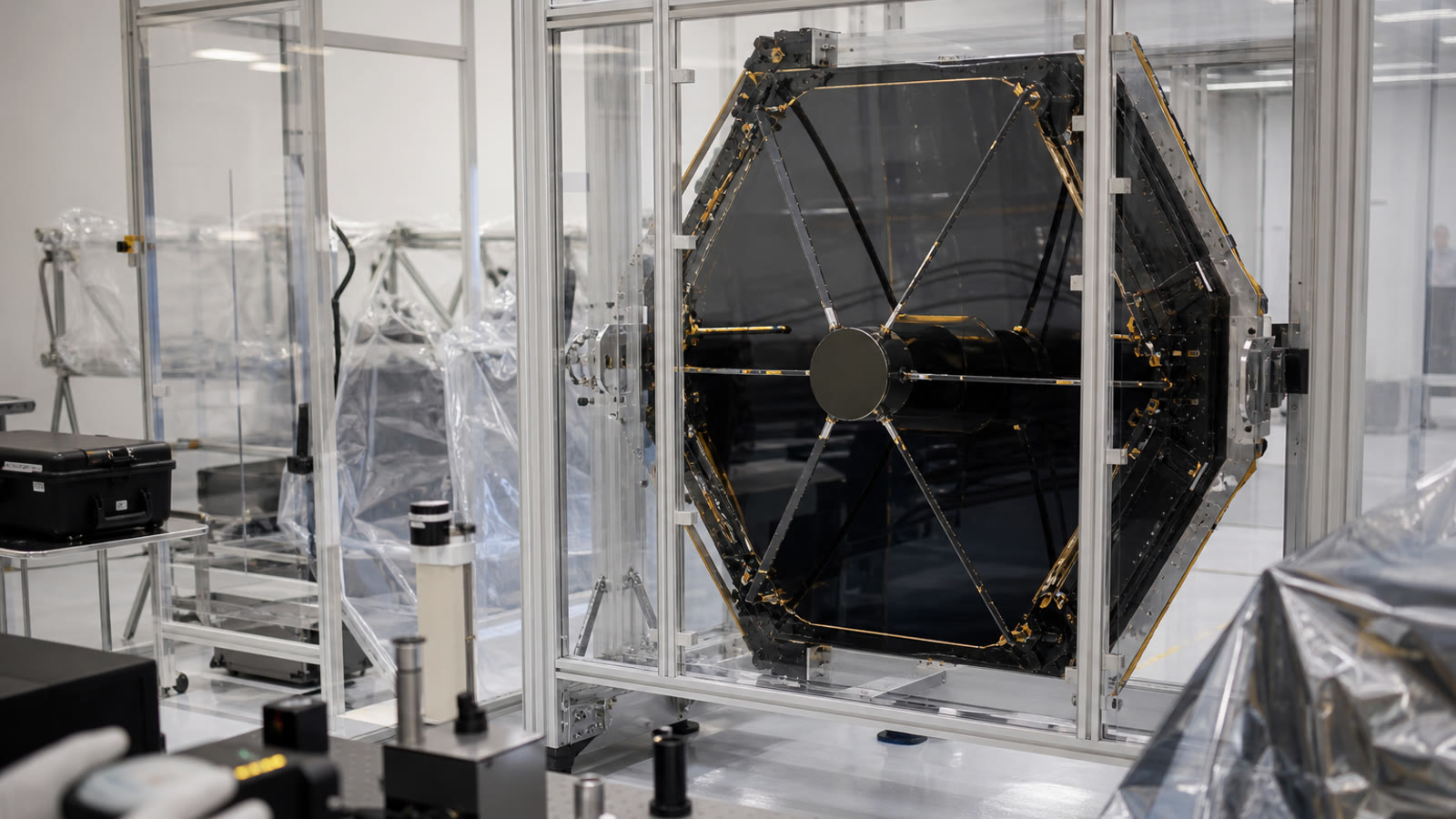 A clean spacecraft integration room with a protected telescope mirror and careful inspection equipment.