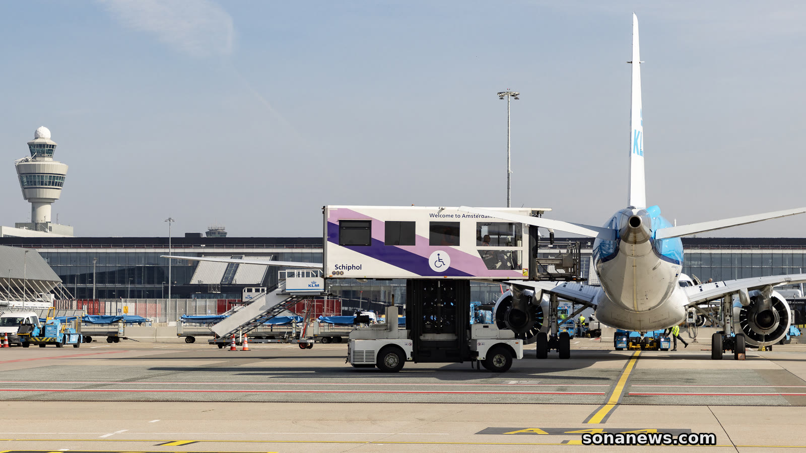 Een Schiphol-voertuig voor reizigers met beperkte mobiliteit staat naast een vliegtuig op het platform.