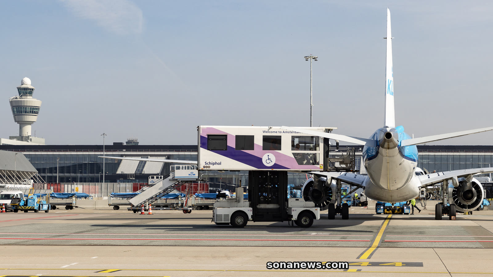 Een Schiphol-voertuig voor reizigers met beperkte mobiliteit staat naast een vliegtuig op het platform.